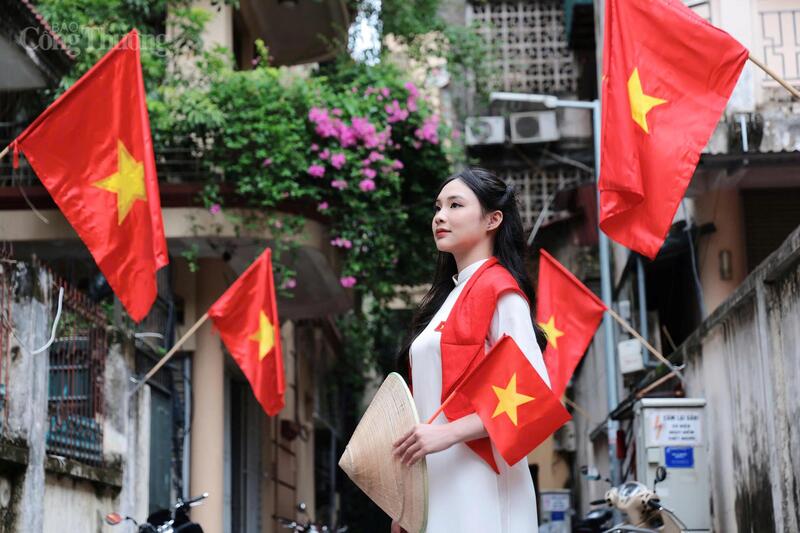 Thiếu nữ trong tà áo dài trắng, cầm cờ đỏ sao vàng, đứng giữa con phố Hà Nội rợp cờ hoa, mang niềm tự hào thế hệ mới