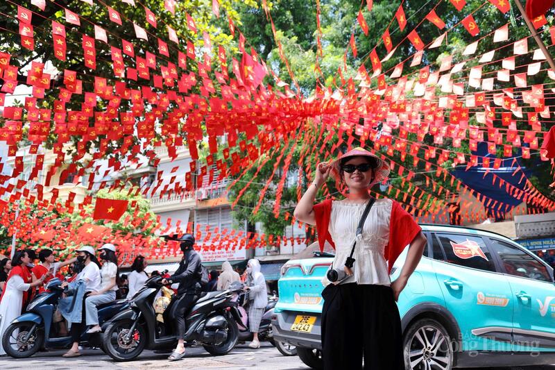 Một thiếu nữ đội nón lá, khoác áo đỏ đứng giữa biển cờ tung bay, hình ảnh dung dị mà giàu biểu tượng