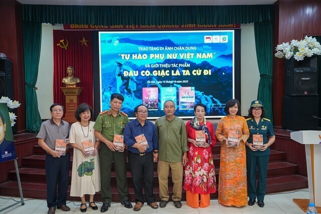 Trao cuốn sách "Đâu có giặc là ta cứ đi" cho thân nhân liệt sĩ Lê Văn Dỵ và các đại biểu dự sự kiện.