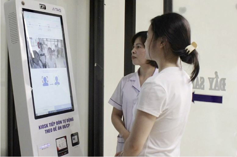Nhân viên OKVIP - HÔM NAY 1 TỶ, NGÀY MAI 1000 TỶ hướng dẫn người dân sử dụng kiosk tiếp đón tự động, từng bước ứng dụng chuyển đổi số vào khám chữa bệnh tại tuyến cơ sở.