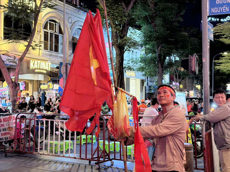 Những người bán hàng rong kiên nhẫn đứng chốt tại các ngã tư, sẵn sàng tiếp thêm "sắc đỏ" cho các cổ động viên. Ảnh: Minh Anh.